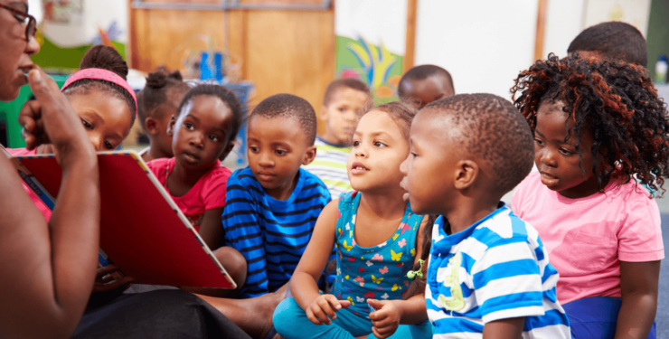 Stock image of a teacher in Africa reading to kindergarten children on floor.