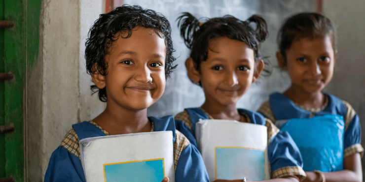 Three smiling girls from India holding school books in classroom