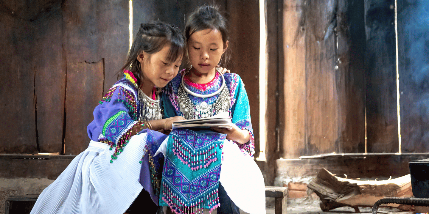Two H'mong girls read a book together near a fireplace in Vietnam.