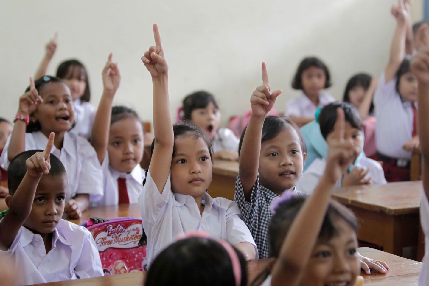 Students in primary school class in Indonesia raise their hands.